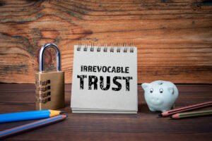 Cardboard notepad with words "irrevocable trust" on wooden texture table.